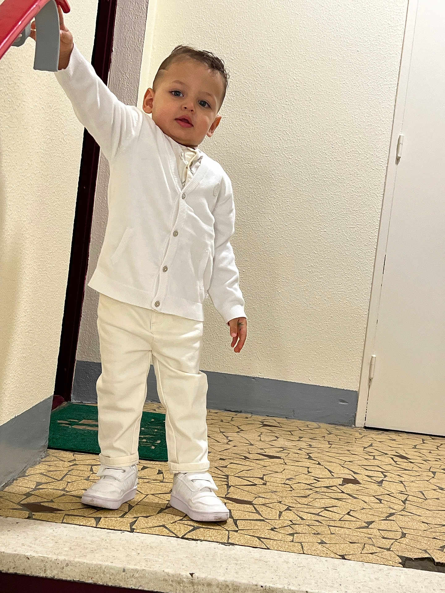 Sami a rejoint le concours — aidez-le/la à gagner de superbes lots ! toddler, child, white_clothing, cardigan, pants, sneakers, indoors, floor, mosaic, railing, hand, door, wall, curious, standing, person, young_child, portrait, footwear, casual