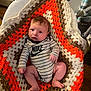 Waylon is registered to the contest to win money with this photo: baby, baby_bassinet, brown, child, cream, crocheted_blanket, cute, handmade, indoor, infant, knitted, newborn, nike, onesie, orange, person, portrait, relaxed, striped_clothing, wooden_floor
