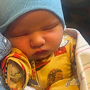 Waylon is registered to the contest to win money with this photo: baby, sleeping, blue_hat, pajamas, blanket, infant, cute, cozy, face, child, newborn, soft_lighting, indoors, resting, peaceful, patterned_clothing, wrapped, closeup, adorable, warm