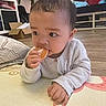 baby, child, curious, cushion, eating, face, floor, food, furniture, hand, home, indoor, living_room, mat, orange, person, sweater, television, wood_floor, young_child