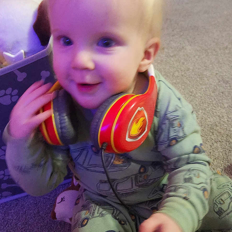Joey is registered to the contest to win money with this photo: baby, bodypart, clothing, coat, couch, cushion, electronics, face, finger, furniture, hand, head, headphones, homedecor, jeans, pants, person, photography, portrait, sitting