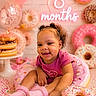 baby, child, infant, pink, donut, sprinkles, balloon, smile, cute, happy, celebration, props, neon_sign, socks, curly_hair, sitting, food_theme, birthday, milestone, playful