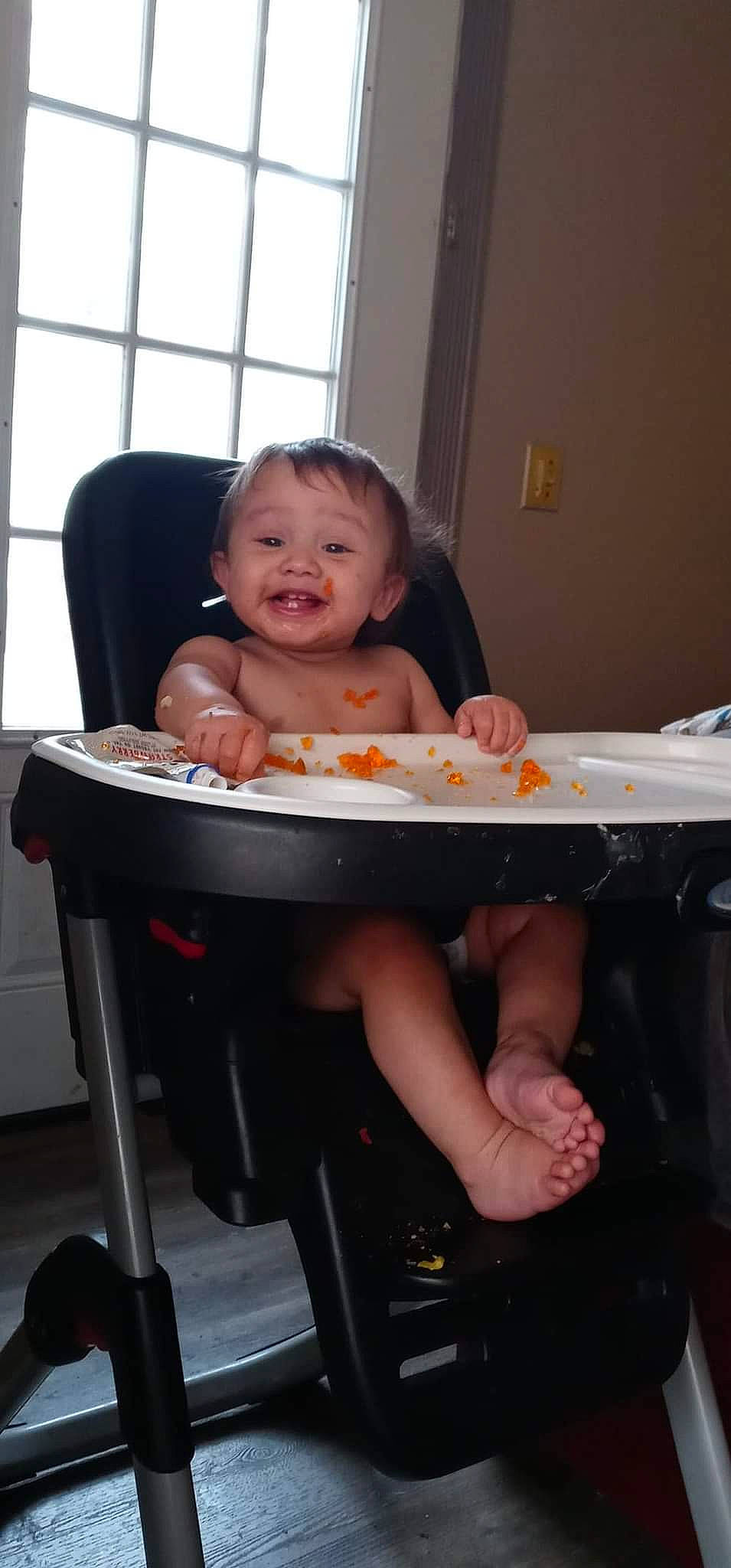 Juan is registered to the contest to win money with this photo: arm, baby, baby_products, baby_toddler_clothing, chair, child, comfort, cooking, curtain, finger, fun, leg, person, room, sitting, smile, standing, table, thumb, toddler