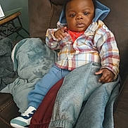 La'Treyveonn is registered to the contest to win money with this photo: baby, blanket, blue_hood, casual_clothing, child, comfortable, couch, cozy, curly_hair, furniture, home_interior, indoor, person, plaid_jacket, portrait, relaxed, seated, sneakers, soft_fabric, young_child