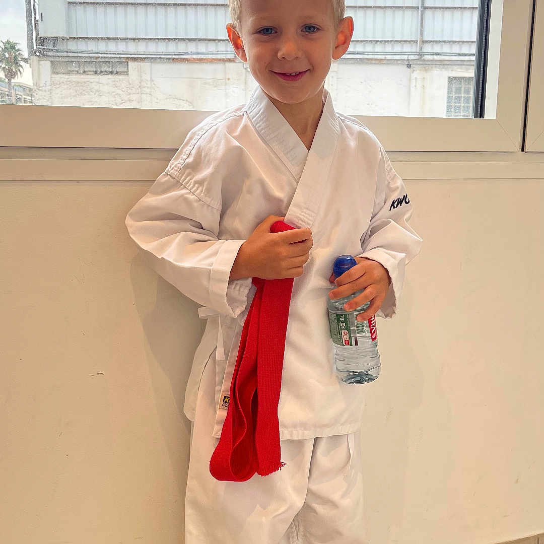 Palchykov Oleksandr a rejoint le concours — aidez-le/la à gagner de superbes lots ! barefoot, blond_hair, boy, casual, child, cloudy_sky, floor_tiles, happy, indoor, karate_gi, martial_arts, portrait, pose, red_belt, smiling, standing, water_bottle, white_clothing, window, young