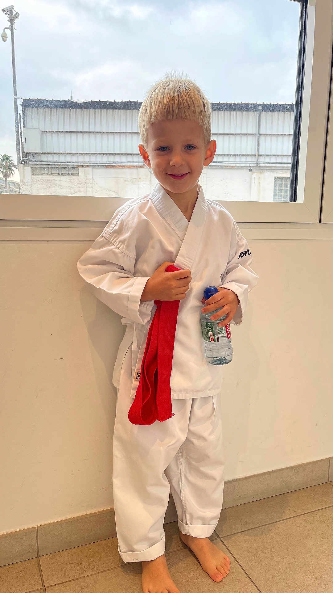 Palchykov Oleksandr a rejoint le concours — aidez-le/la à gagner de superbes lots ! child, boy, karate_gi, red_belt, water_bottle, barefoot, indoor, window, cloudy_sky, smiling, blond_hair, martial_arts, pose, floor_tiles, casual, young, portrait, standing, white_clothing, happy