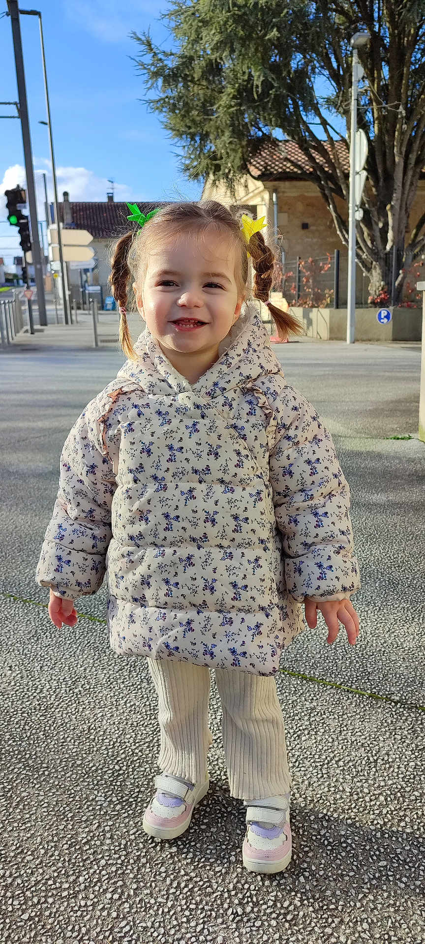 Lily a rejoint le concours — aidez-le/la à gagner de superbes lots ! child, girl, smiling, pigtails, hair_clips, jacket, floral_pattern, pants, sneakers, outdoor, sidewalk, daylight, tree, street, building, happy, cute, portrait, standing, urban