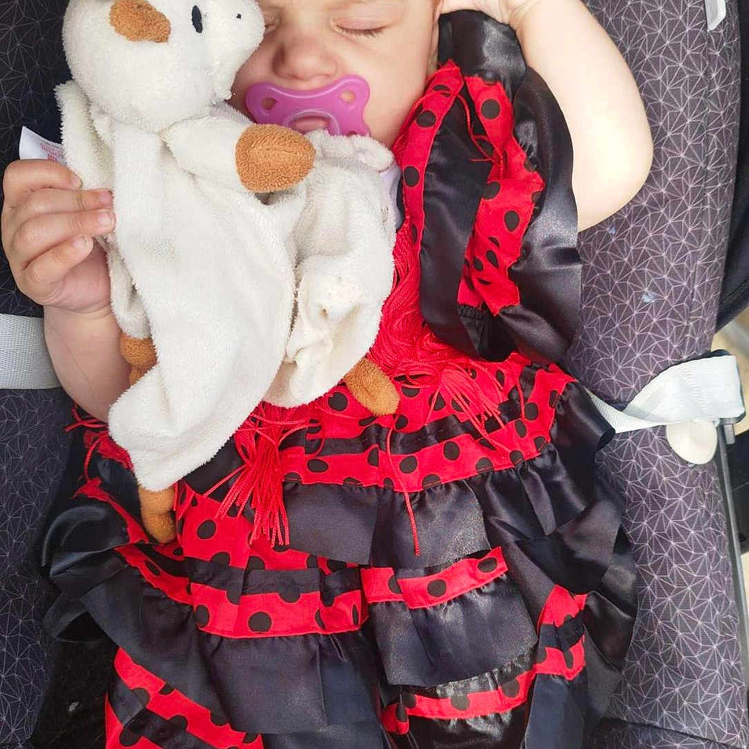 Giulia participe au concours pour gagner de l'argent avec cette photo : baby, black, car_seat, child, comfort, cute, dress, fabric, foot, hand, indoor, infant, pacifier, peaceful, plush_toy, polka_dot, red, resting, safety_label, sleeping