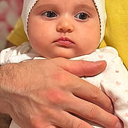 Emma joined the competition — help win amazing prizes! baby, infant, hand, white_bonnet, heart_pattern, clothing, person, adult_hand, closeup, portrait, skin, face, cute, expression, soft_lighting, indoor, holding, newborn, toddler, human
