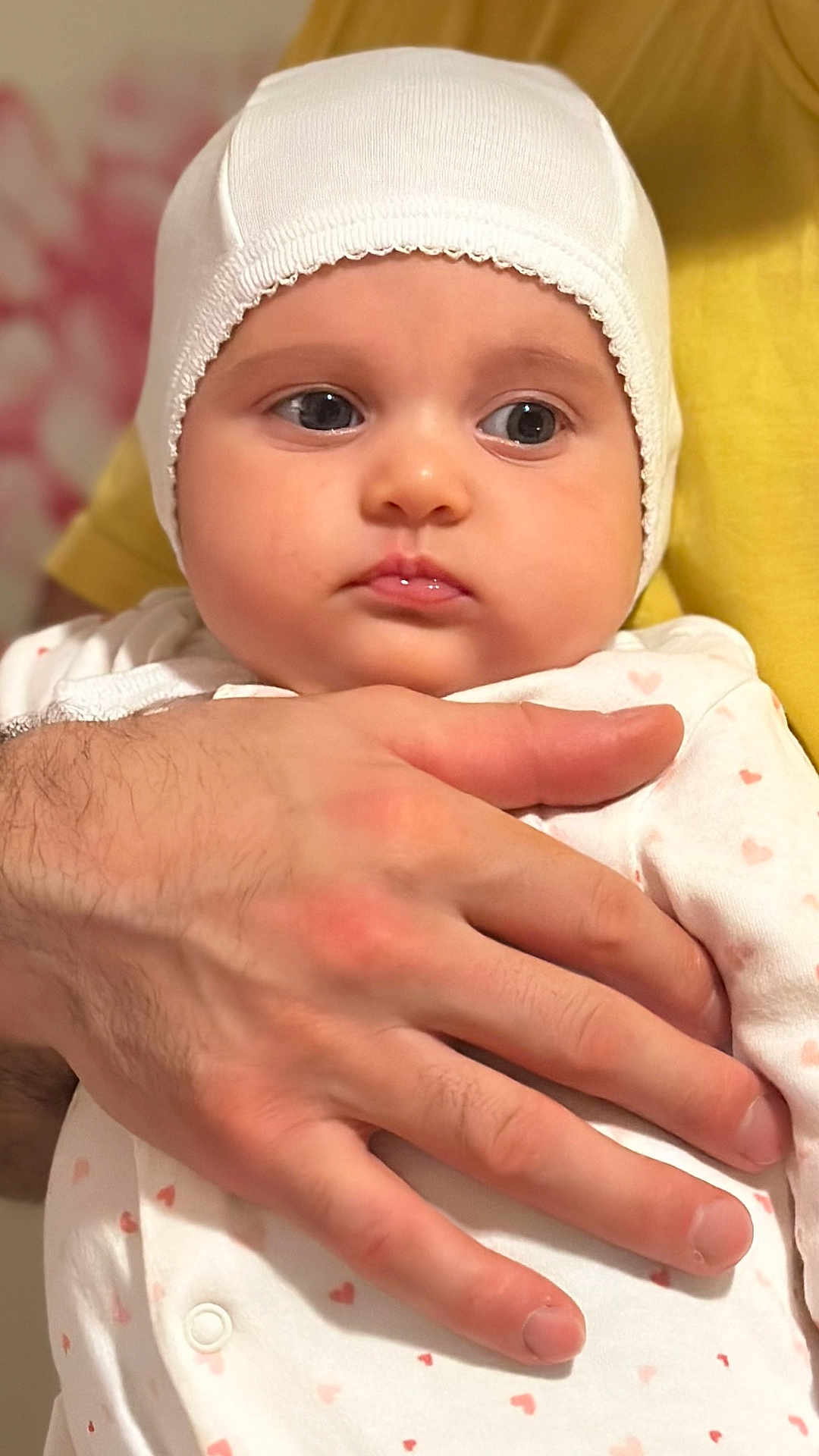 Emma joined the competition — help win amazing prizes! baby, infant, hand, white_bonnet, heart_pattern, clothing, person, adult_hand, closeup, portrait, skin, face, cute, expression, soft_lighting, indoor, holding, newborn, toddler, human