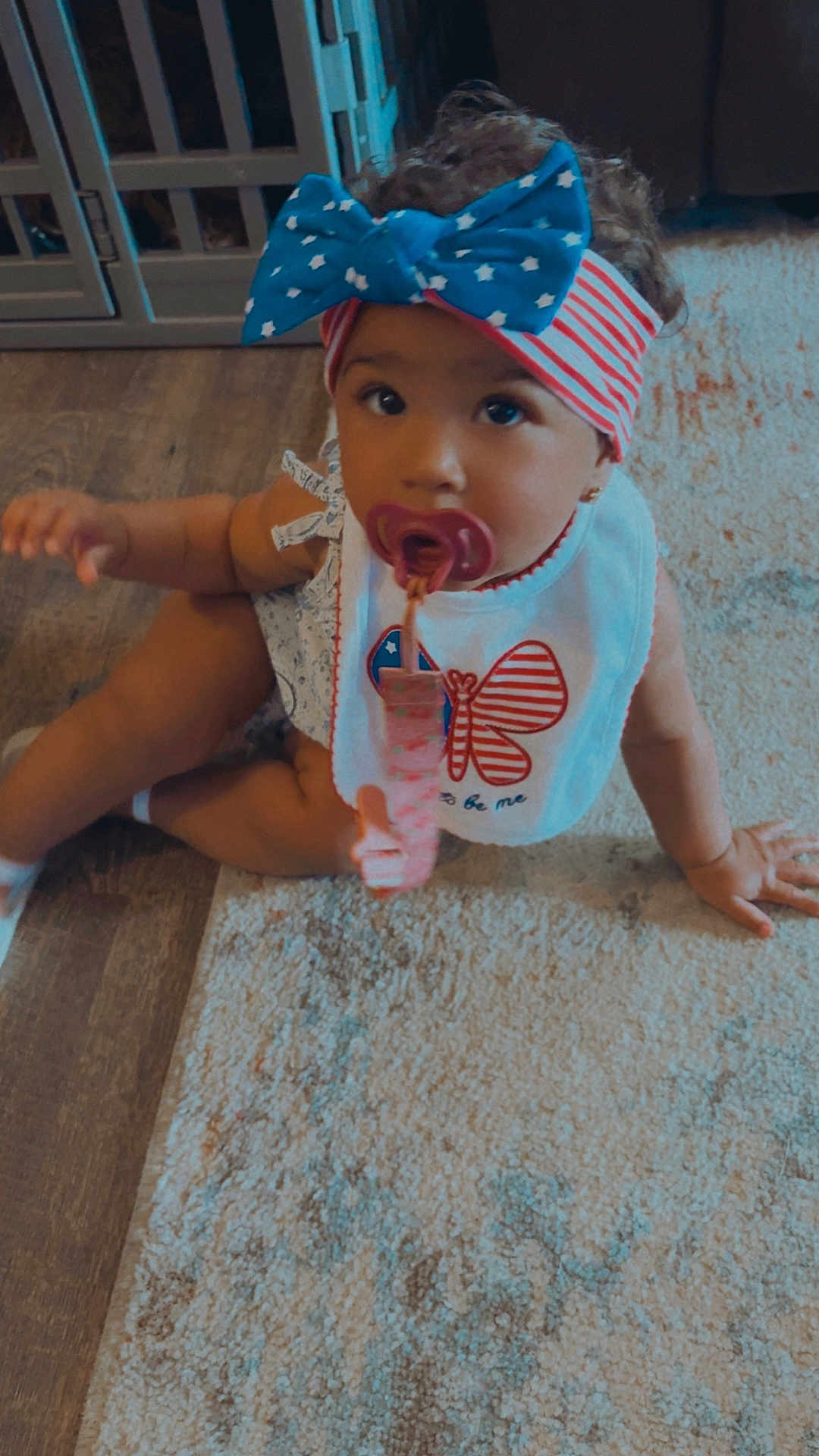 Zariyah is registered to the contest to win money with this photo: toddler, child, pacifier, headband, bow, bib, butterfly, carpet, rug, floor, indoor, curly_hair, clothing, sitting, baby, person, cute, looking_up, infant, home