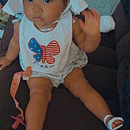 Zariyah is registered to the contest to win money with this photo: baby, child, hat, bib, butterfly, american_flag, pacifier, pacifier_clip, sitting, couch, footwear, sandals, waving, indoors, person, cute, clothing, accessory, face, expression