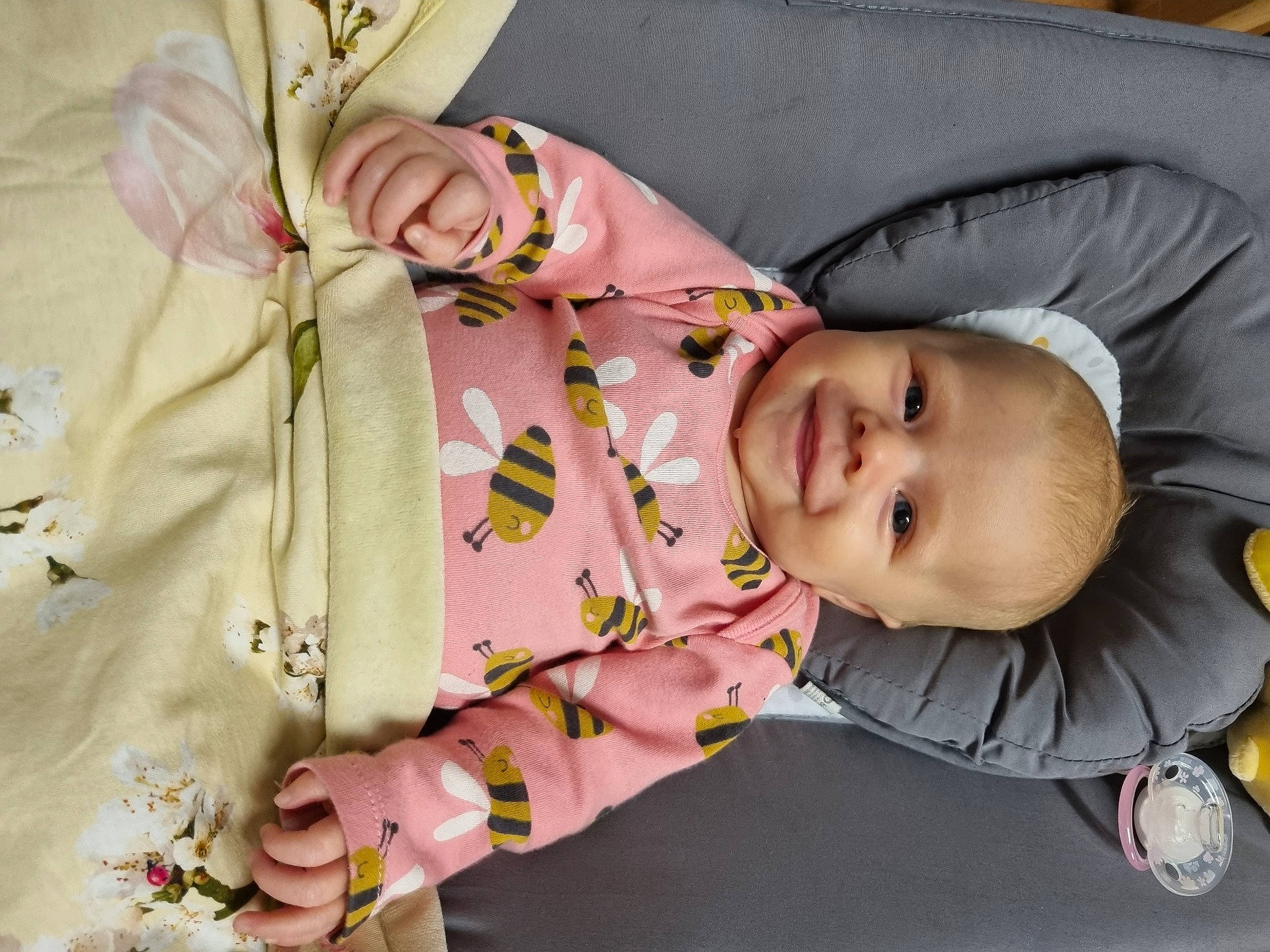 Phoebe is registered to the contest to win money with this photo: baby, baby_products, baby_toddler_clothing, cheek, child, comfort, fashion_accessory, happy, human, human_body, joy, mouth, pattern, person, room, rose, sitting, skin, sleeve, smile