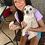 girl, child, dog, pet, smile, sitting, chair, indoor, casual, holding, food, shorts, purple_shirt, small_dog, brown_eyes, wet_hair, table, cooler, concrete_floor, relaxed
