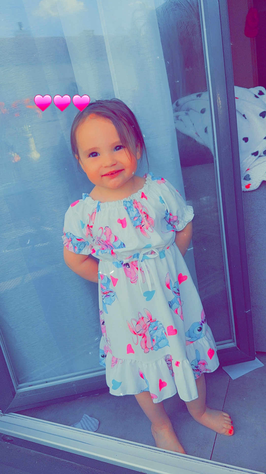 Sydney a rejoint le concours — aidez-le/la à gagner de superbes lots ! toddler, child, dress, barefoot, smiling, heart_emoji, glass_door, floor, tile, curtain, indoor, cartoon_print, pink_hearts, happy, standing, cute, girl, portrait, colorful, casual
