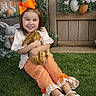 child, girl, smiling, rabbit, animal, grass, bow, orange, white_shoes, plaid_pants, lace, flower_arrangement, decorative_eggs, wooden_background, indoor_garden, cute, happy, sitting, toy, portrait