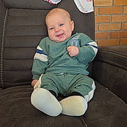 Steven joined the competition — help win amazing prizes! baby, infant, smiling, recliner, chair, green_tracksuit, soft_shoes, blanket, muslin, brick_wall, indoors, portrait, sitting, cute, happy, hand, face, head, cozy, nursery