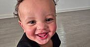 Caius is registered to the contest to win money with this photo: toddler, child, smile, happy, curly_hair, indoor, floor, window, blinds, black_shirt, person, baby, closeup, portrait, candid, joyful, skin, face, young_child, home