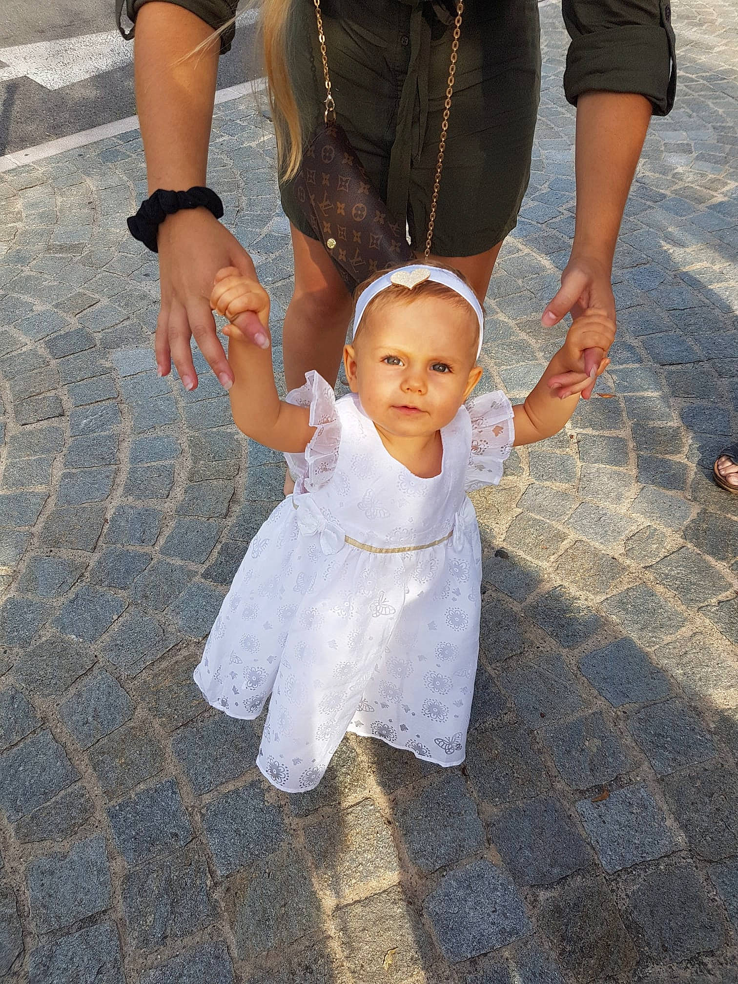 Mathilde a rejoint le concours — aidez-le/la à gagner de superbes lots ! asphalt, dress, event, flooring, foot, gesture, hand, happy, holding_hands, human_leg, leg, people, person, road_surface, sandal, shoe, sidewalk, toddler, tradition, tree