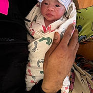Royal is registered to the contest to win money with this photo: newborn, baby, infant, wrapped, blanket, footprint_pattern, hat, striped_hat, hand, holding, person, indoor, wood_floor, clothing, cute, face, portrait, warm, care, toddler
