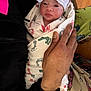 newborn, baby, infant, wrapped, blanket, footprint_pattern, hat, striped_hat, hand, holding, person, indoor, wood_floor, clothing, cute, face, portrait, warm, care, toddler
