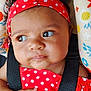 Royal is registered to the contest to win money with this photo: baby, child, infant, red_headband, red_dress, polka_dot, curly_hair, face, hand, black_harness, floral_pattern, colorful_background, sitting, portrait, closeup, skin, expression, cute, indoors, person