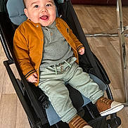 Ishaq a rejoint le concours — aidez-le/la à gagner de superbes lots ! baby, child, stroller, smile, happy, jacket, cardigan, knit_top, green_pants, brown_shoes, sneakers, seat, indoor, wood_floor, metal_table, hand, face, eyes, cheeks, portrait