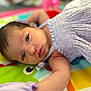 baby, infant, face, arm, purple_clothing, play_mat, colorful, lying_down, skin, eyes, head, newborn, soft_texture, cute, person, child, young, indoors, closeup, expression