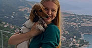 Bailey participe au concours pour gagner de l'argent avec cette photo : woman, person, puppy, dog, long_eared_dog, smiling, portrait, outdoor, sunset, coastal_view, mountains, town, ocean, bay, balcony, glass_railing, green_dress, blonde_hair, holding_dog, travel