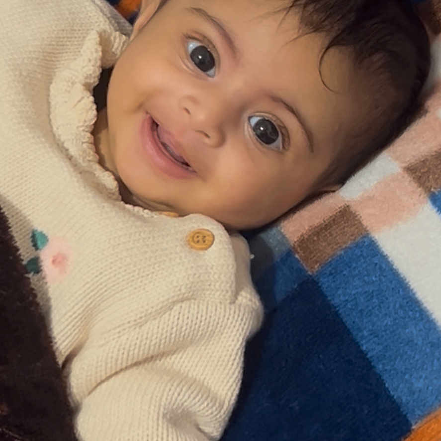 Rehmat Kaur joined the competition — help win amazing prizes! baby, blanket, cheerful, child, closeup, colorful, cozy, cute, face, happy, indoors, infant, knitted_clothing, lying_down, portrait, smiling, striped, sweater, warm, young_child