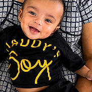 Niyansh joined the competition — help win amazing prizes! baby, child, smile, happy, face, person, clothing, black_shirt, yellow_text, sitting, lap, adult_arm, patterned_clothing, portrait, indoor, cute, joy, young_child, head, skin