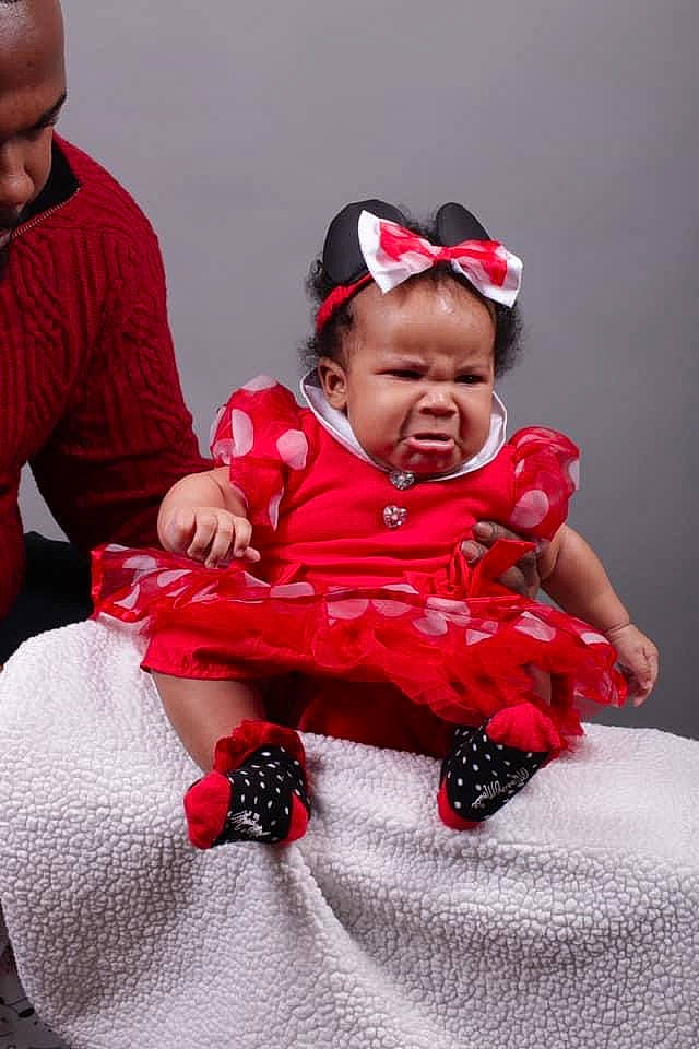 Arizona is registered to the contest to win money with this photo: baby, baby_toddler_clothing, carmine, child, costume, costume_accessory, embellishment, face, hair_accessory, headband, headpiece, mouth, nose, person, photo_shoot, pink, red, sitting, toddler