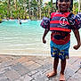 child, smiling, pool, swim_vest, swim_trunks, barefoot, water, outdoor, tropical, palm_trees, playful, happy, summer, vacation, people, recreation, sunlight, fun, holiday, posing