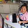 Xiomara is registered to the contest to win money with this photo: child, smiling, girl, medical_equipment, keyboard, desk, communication_device, hospital_room, chair, pink_shirt, healthcare, technology, monitor, cable, bottle, happy, indoor, patient, therapy, positive