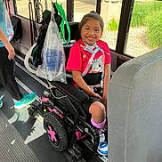 Xiomara joined the competition — help win amazing prizes! child, wheelchair, bus, smiling, girl, bright_clothing, cat_print, purple_socks, medical_equipment, ventilator, window, sunlight, greenery, floor, seat, person, happy, transportation, indoor, shoes
