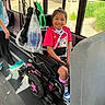child, wheelchair, bus, smiling, girl, bright_clothing, cat_print, purple_socks, medical_equipment, ventilator, window, sunlight, greenery, floor, seat, person, happy, transportation, indoor, shoes
