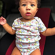 Heaveniyah joined the competition — help win amazing prizes! baby, child, curly_hair, onesie, floral_pattern, sitting, seat, red, black, expression, face, legs, arms, indoors, portrait, cute, young, skin, person, infant