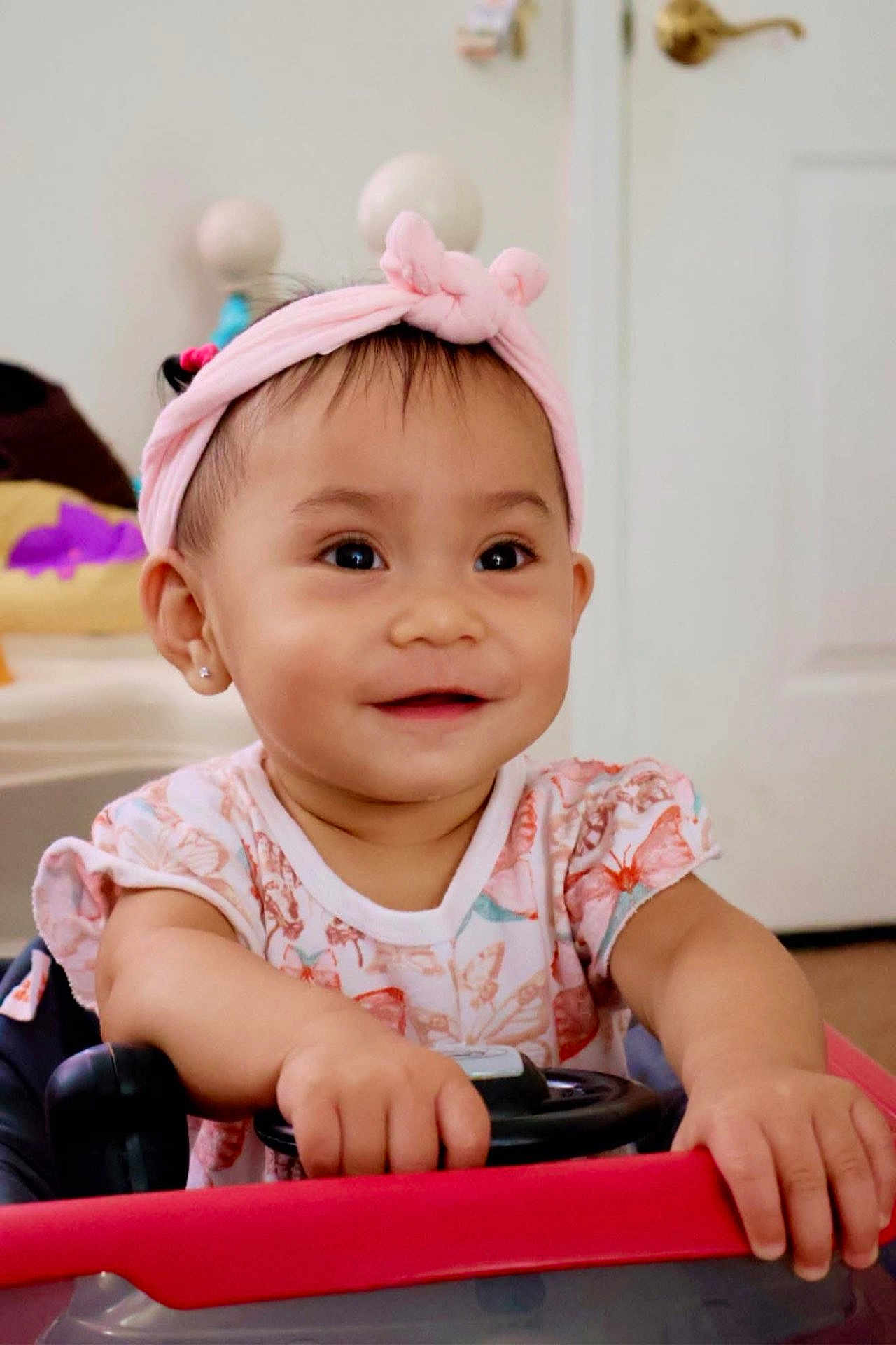 Felizia Rae joined the competition — help win amazing prizes! toddler, child, baby, headband, pink, smile, indoor, toy_car, hands, face, cute, eyes, clothing, playing, happy, young_child, person, infant, portrait, home