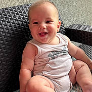 Hansel is registered to the contest to win money with this photo: baby, smiling, sitting, cushion, wicker_chair, tank_top, indoor, happy, child, infant, cute, pattern, furniture, skin, person, portrait, young, plump, hand, foot