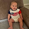 Hansel is registered to the contest to win money with this photo: baby, infant, child, couch, sofa, onesie, american_flag, indoor, furniture, smile, face, person, sitting, cute, happy, skin, head, leg, foot, home