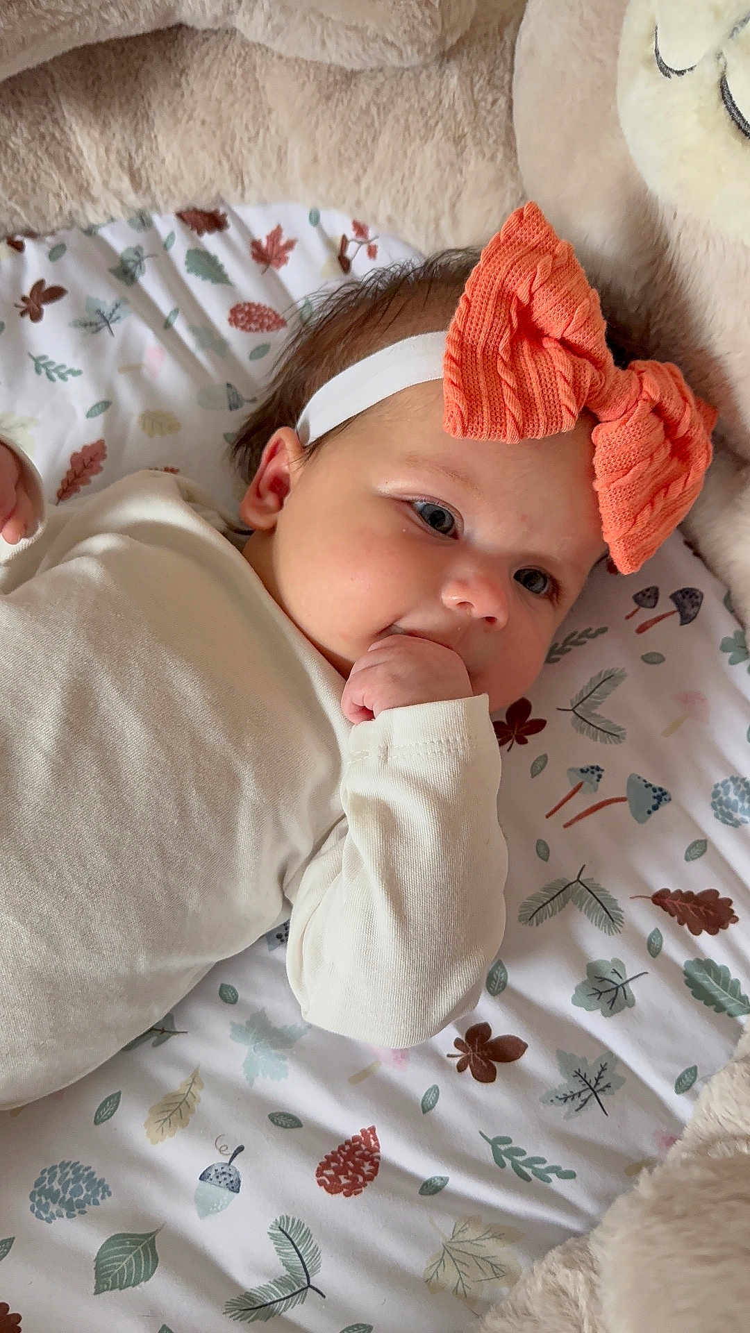 Elara is registered to the contest to win money with this photo: baby, infant, headband, bow, hand, blanket, pattern, leaf, mushroom, cute, lying_down, soft_texture, cozy, child, face, clothing, white_outfit, indoors, portrait, toddler