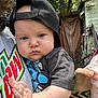 baby, child, face, cap, black_cap, tshirt, hand, person, outdoor, backyard, shed, greenery, drink, cup, holding, expression, casual_clothing, summer, daylight, portrait