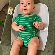 Theodore is registered to the contest to win money with this photo: baby, infant, green_onesie, baby_seat, child, cute, smiling, indoor, carpet, fabric, mesh, hand, foot, face, skin, person, newborn, happy, sitting, toddler