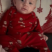 Liridon joined the competition — help win amazing prizes! baby, infant, child, red_pajamas, holiday_pattern, pillow, cushion, couch, sitting, indoor, portrait, face, eyes, ears, socks, feet, hands, cozy, adorable, neutral_expression