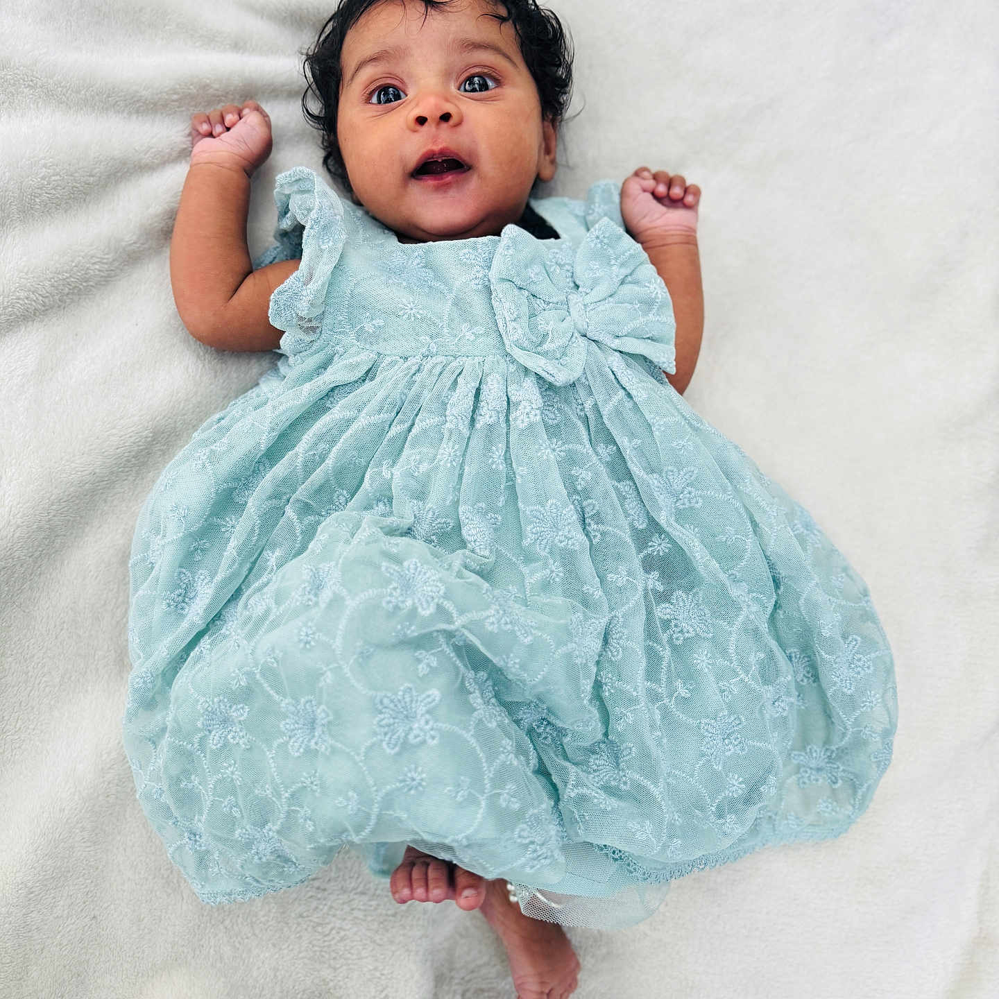 Shreevamika is registered to the contest to win money with this photo: adorable, baby, bare_feet, blanket, blue_dress, child, cute, expression, fabric, hands_up, indoors, infant, lace, lying_down, newborn, person, portrait, ruffles, soft_texture, wide_eyes