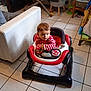 Adrien a rejoint le concours — aidez-le/la à gagner de superbes lots ! toddler, baby_walker, child, striped_shirt, indoor, living_room, tile_floor, furniture, chair, table, toy, person, floor, curious, seated, home, casual, young_child, walker, red