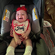 Nova is registered to the contest to win money with this photo: baby, infant, car_seat, bib, headband, socks, smiling, happy, indoor, clothing, red, white, striped, face, person, child, seat, leather_couch, baby_gear, footwear