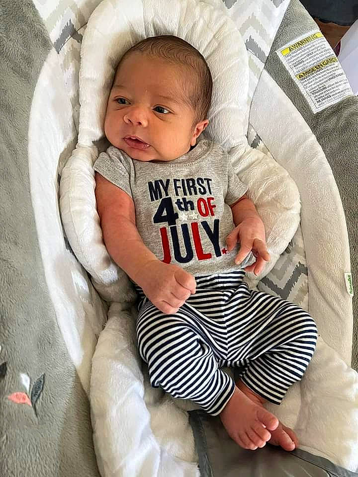 Maverick is registered to the contest to win money with this photo: baby, baby_products, baby_toddler_clothing, child, comfort, couch, eye, hairstyle, knee, linens, pattern, person, pillow, sitting, sleeve, sock, t_shirt, textile, thigh, throw_pillow