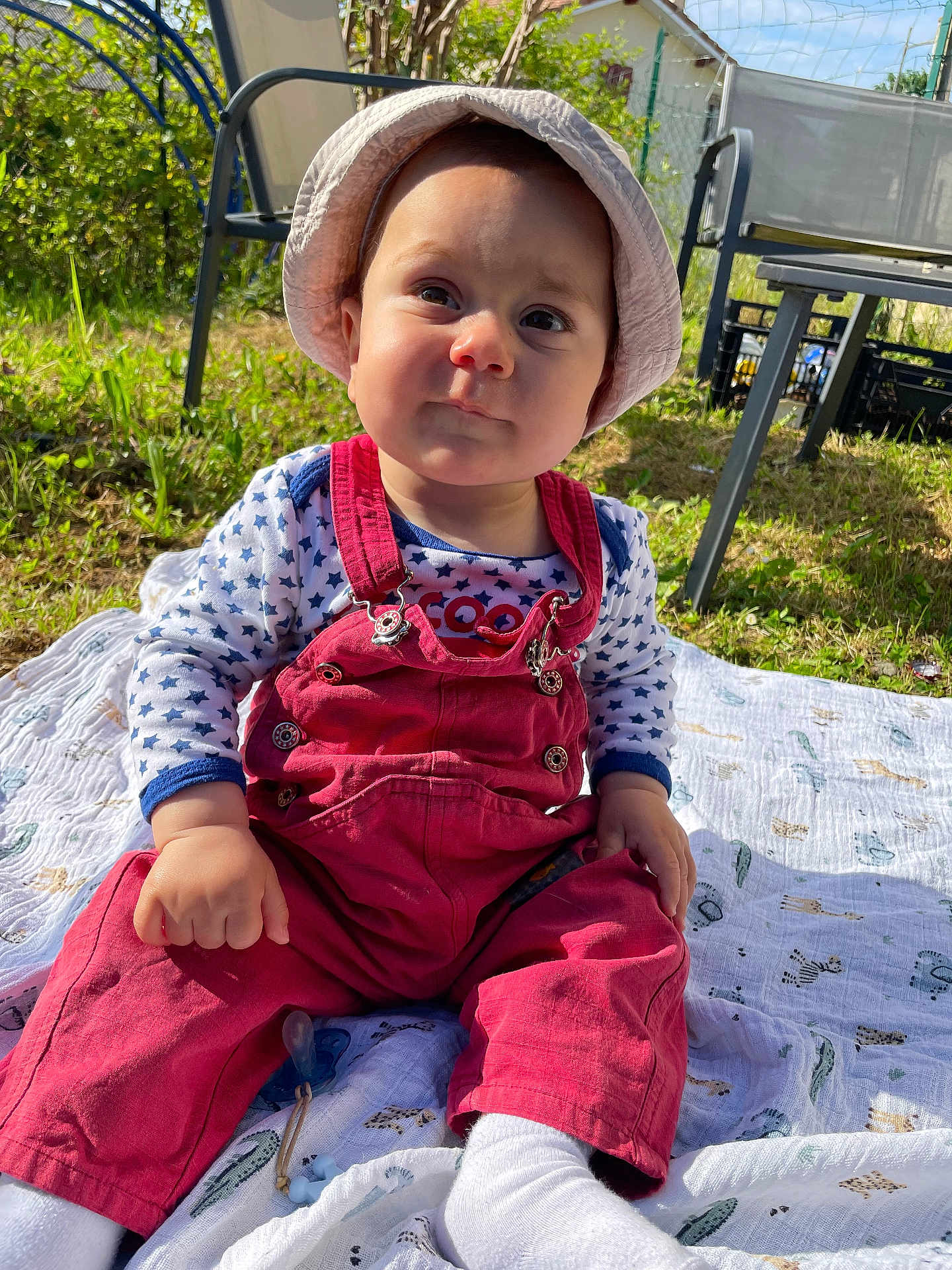 Alessio participe au concours pour gagner de l'argent avec cette photo : baby, child, outdoor, grass, blanket, hat, overalls, sunlight, garden, chair, greenery, face, sitting, expression, white_socks, patterned_blanket, daylight, nature, person, cute