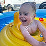 baby, child, smiling, laughing, inflatable_pool, yellow_float, water, wet_hair, outdoor, summer, toy, van, vehicle, sunlight, happy, skin, arm, head, face, play